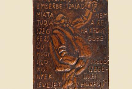 Szabolcs Péter bronz plakettje, melyen József Attila: Ős patkány terjeszt kórt című versének sorai és a költő monogramja olvasható