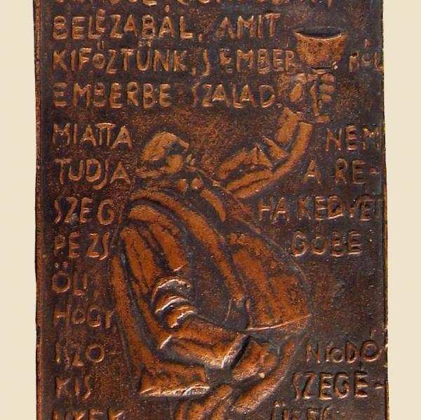Szabolcs Péter bronz plakettje, melyen József Attila: Ős patkány terjeszt kórt című versének sorai és a költő monogramja olvasható